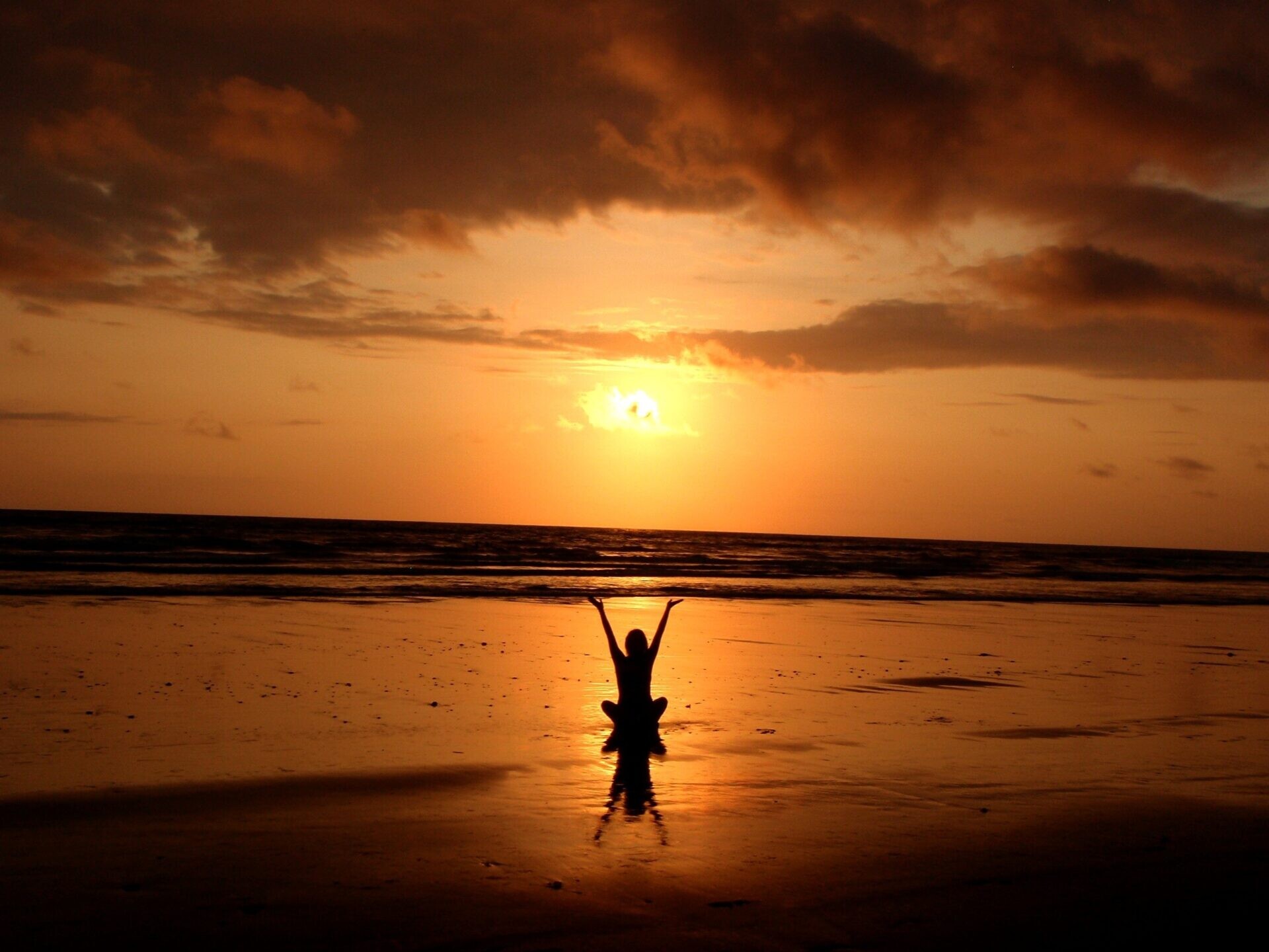 A woman meditates on a Jamaican beach with the sun setting in the background, promoting the benefits of psilocybin retreats.